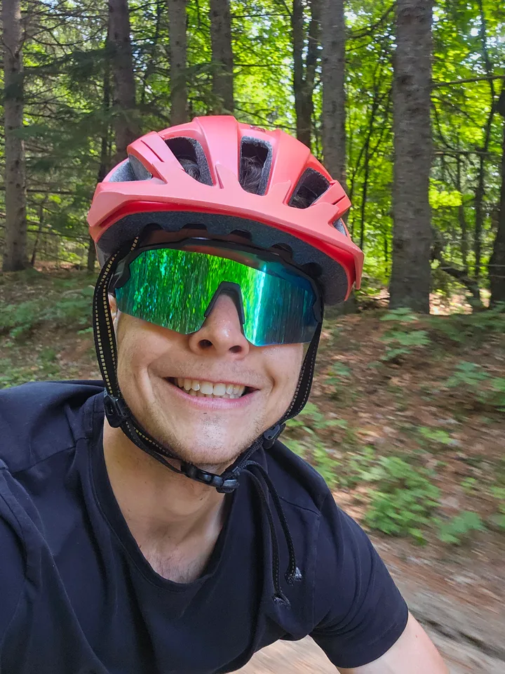 Smiling while cycling through a wooded trail in a helmet and sunglasses